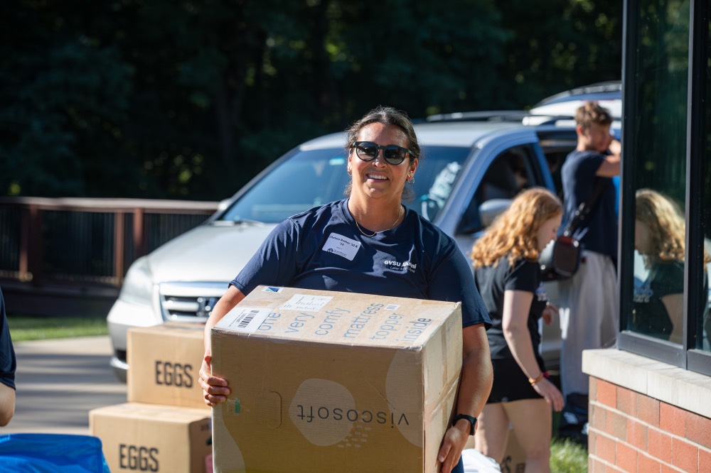 GVSU Alumna smiles as she carries in a big cardboard box